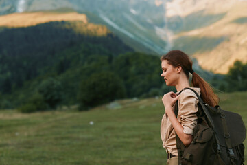 Fototapeta premium Woman hiking outdoors with backpack, looking ahead, natural light, lush landscape, distant mountains, calm moment, casual clothing, adventure vibe