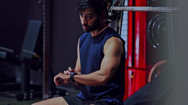 Fitness gym workout athlete smartwatch training muscular man sport exercise, muscular man checking smartwatch during gym workout, focused athlete resting bench near weight equipment, strength routine