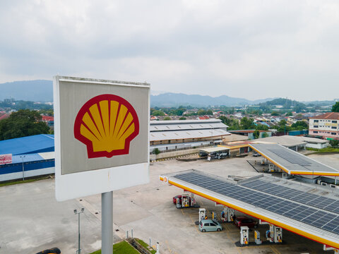 Aerial view of a Shell petrol station with fuel pumps and branding signage beside a commercial area in Malaysia.