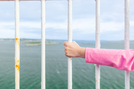 Kinderhand h&auml;lt sich an Gitterstange fest mit Ausblick auf das Meer.