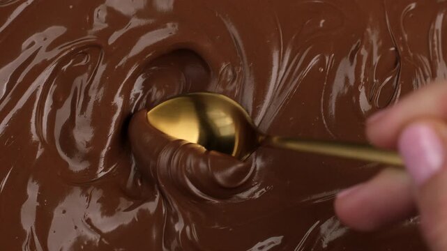 Mixing melted chocolate with a spoon, close up. Smooth glossy texture of chocolate