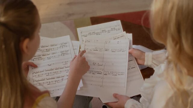 High angle view of female teacher and Caucasian female child studying sheet music together during home lesson. Ideal for promoting private tutoring, music schools, and childhood education programs