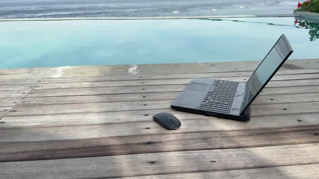 Open laptop by infinity swimming pool with sea view