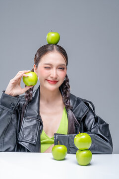 Playful Asian woman in leather jacket with green apples for creative nutrition diet marketing campaign street fashion aesthetic healthy lifestyle pop culture dynamic portrait