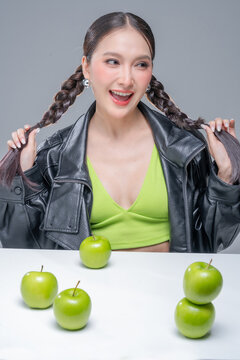 Excited Asian woman holding green apples by braids for dynamic nutrition diet marketing campaign neon street fashion aesthetic healthy lifestyle vibrant portrait studio