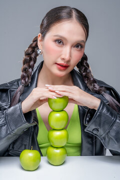 Confident Asian woman balancing tower of green apples for creative nutrition diet marketing campaign neon street fashion aesthetic healthy lifestyle conceptual portrait studio