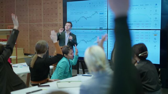 A speaker with Down Syndrome actively presents financial data to an engaged audience of colleagues. Businesspeople raise their hands, participating in the interactive presentation on market trends