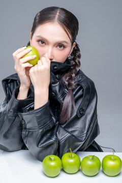 Intense Asian woman hiding face in leather jacket with green apples for creative cosmetics skincare marketing campaign edgy street fashion aesthetic healthy organic nutrition portrait