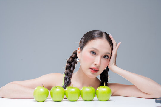 Confident Asian woman behind row of green apples for botanical cosmetics skincare marketing campaign neon street fashion aesthetic healthy lifestyle premium organic nutrition portrait stock