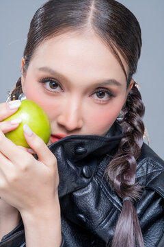 Intense Asian woman hiding face in leather jacket with green apples for creative cosmetics skincare marketing campaign edgy street fashion aesthetic healthy organic nutrition portrait