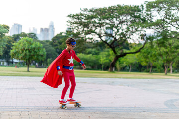 Fototapeta premium Child in superhero costume skateboards in a park with city skyline.