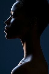 Fototapeta premium Profile portrait of a young African woman with short hair illuminated against a dark background, showcasing her facial features and elegant neck in low-key lighting