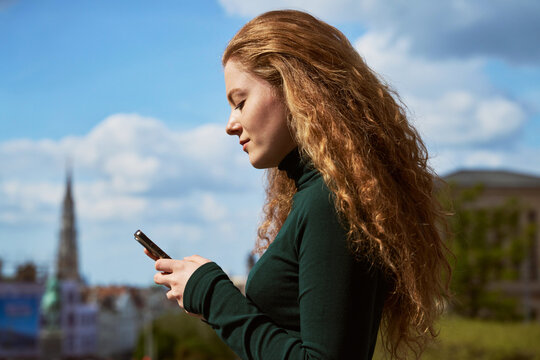 Woman Using Smartphone in City With Buildings in Background