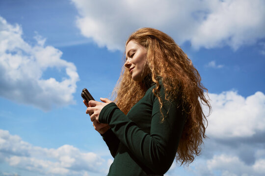 Woman Using Smartphone Outdoors Under Blue Sky With Clouds