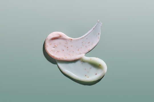 Two cosmetic cream textures with exfoliating particles on a green