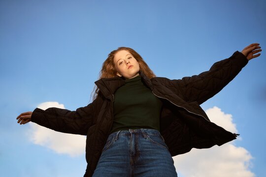 Woman Stands With Arms Outstretched Under Clear Blue Sky