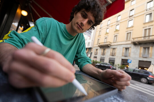 Young man sits at cafe table while using tablet in Italy