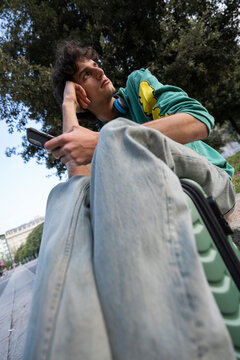 Gen z guy resting with luggage in Italy while using phone