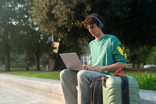 Gen z guy using laptop while sitting on bench in Italy