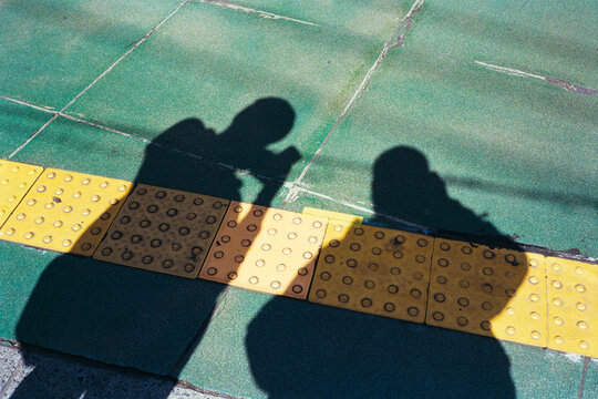 Two Shadows on a Street with Tactile Yellow Tiles