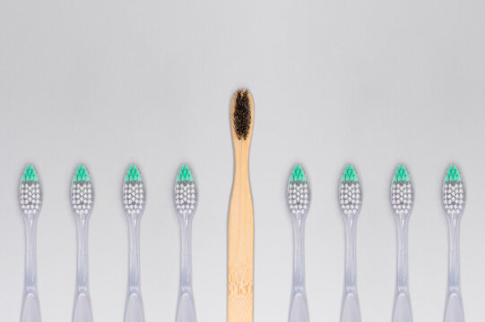 Bamboo toothbrush standing above plastic toothbrushes in row sustainability concept