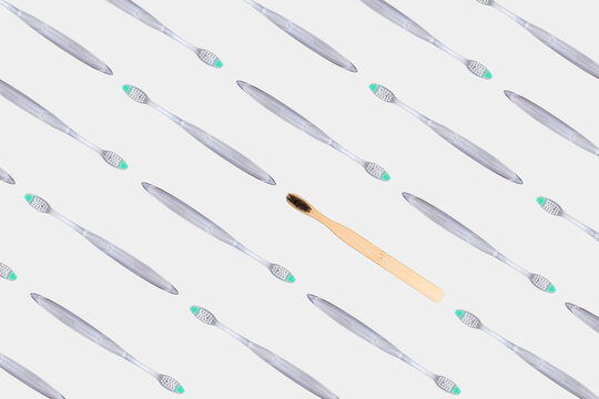 Bamboo toothbrush standing out from transparent plastic toothbrush pattern on gray background