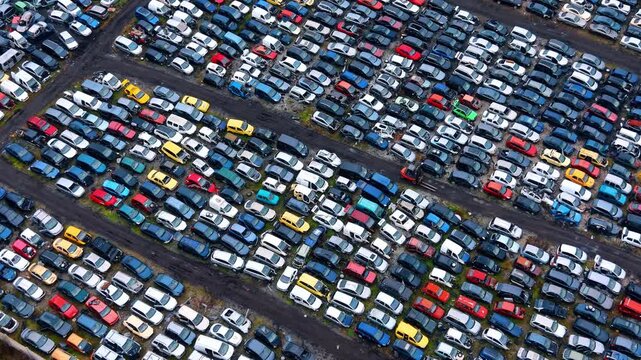 Cars parked in rows at a car junkyard. Many cars are parked close together in a junkyard. The scene shows a variety of colors and models.