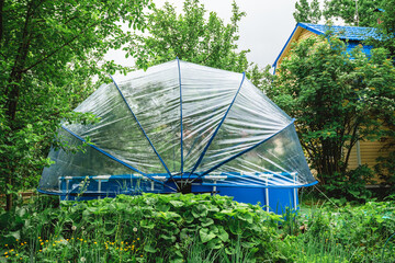 Blue above ground swimming pool enclosed by a transparent dome cover, providing protection and extending the swimming season in a lush green garden during summer © iloli