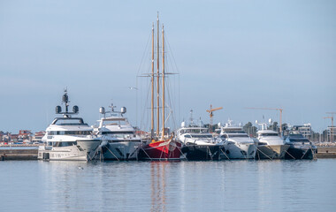 Fototapeta premium Classic Three Masted Sailing Yacht Moored Between Modern Motor Yachts in Harbor