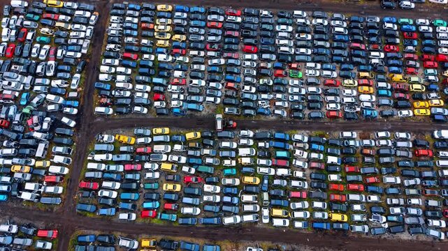 Endless rows of cars in a junkyard. Many cars sit in rows at a junkyard. Different colors and models are scattered across the ground during daylight.