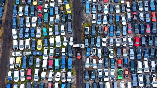 Top down aerial view of scrapyard with working forklift. Direct overhead view of rows of crushed vehicles and a red forklift moving a car down the middle pathway.