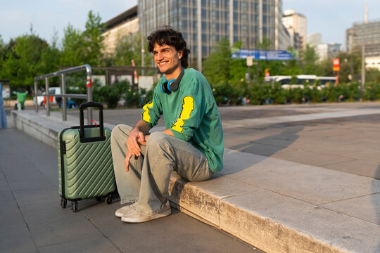 Young man sits on a step with luggage in an Italian city