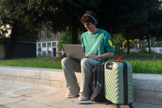 Gen Z guy working on laptop in Italy with trolley nearby