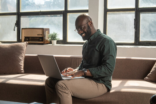 Smiling Man Working Remotely on Laptop at in Sunlit Workplace