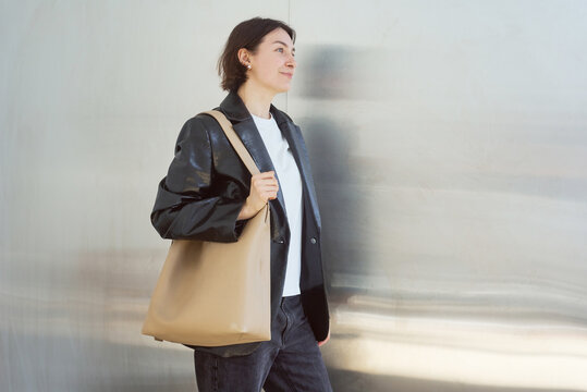 Woman walks past shiny wall carrying a large beige bag