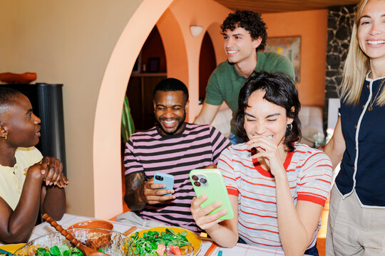 Friends laughing together while using smartphones at lunch