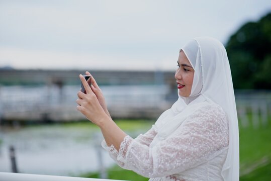 Asian person in a cream hijab taking a photo with a phon
