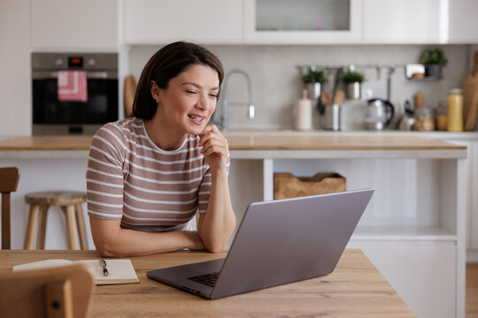 Woman Working on Laptop at home sitting in Kitchen having a video call