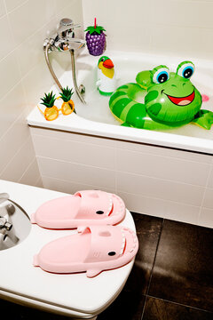 pink shark slides on a bidet lid beside a bathtub with inflatables