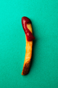 a single french fry with ketchup on a green background