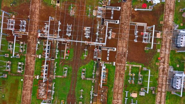 Top down aerial view of electrical substation power grid infrastructure. Direct overhead drone shot of an electrical substation showing transformers, wiring, and steel framework on ground.
