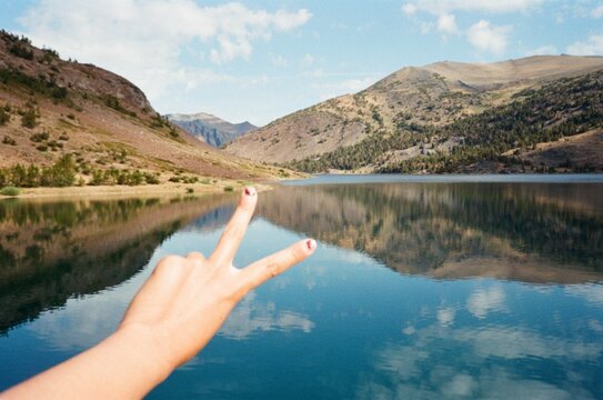 tourist peace sign hand scenic alpine lake with mountains reflection 