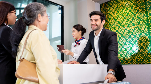  Smiling male receptionist in elegant suit welcoming an elderly Asian female guest at a modern hotel reception desk representing premium customer service and hospitality management