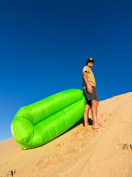 Smiling Man Drags a Green Air Filled Seat Up a Sand Dune