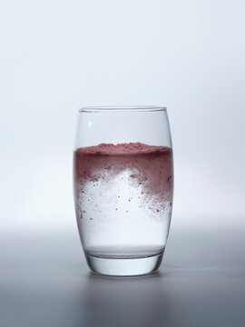 Pink powder dissolving in clear water inside a glass