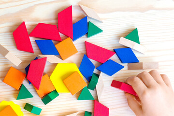Colorful wooden geometric shapes scattered on a light wooden surface with a child's hand reaching for a red piece among the vibrant collection © Nizoli