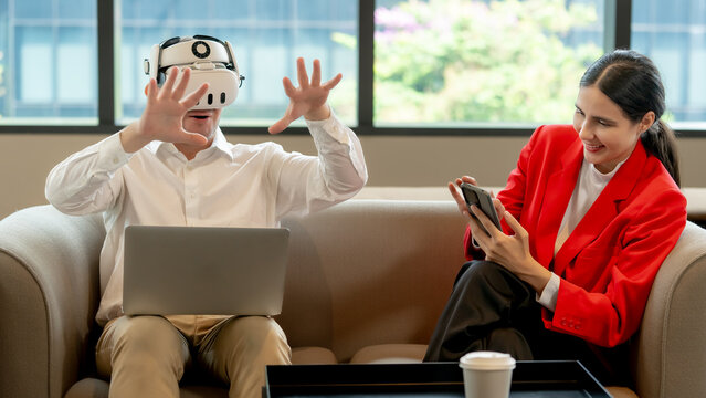 Creative tech partners testing innovative VR metaverse simulation and software applications with laptop and mobile phone inside a modern bright office lounge environment