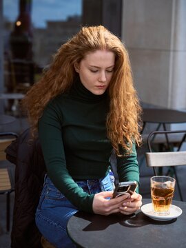 Woman Uses Smartphone at Cafe Table in City During Daytime