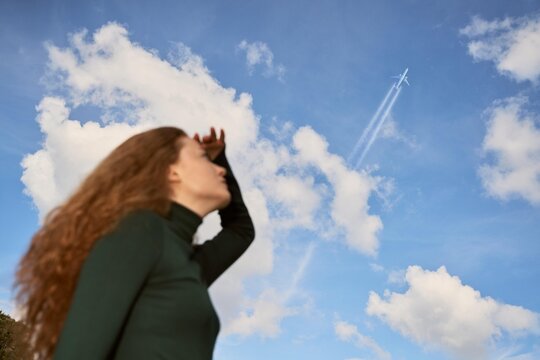 Woman Looks up at Airplane While Standing Under Blue Sky With Clouds