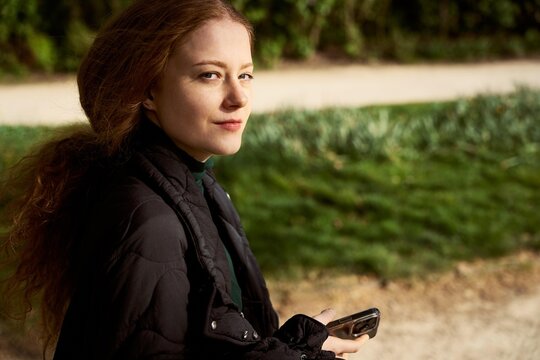 Young Woman Holds Phone While Standing in Park